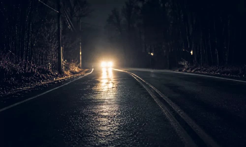 Headlights reflect across an empty wet road at night.