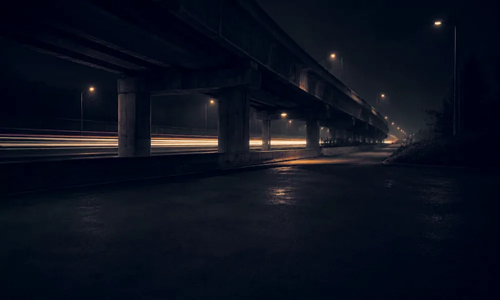 Light trails pass beneath a highway overpass at night.