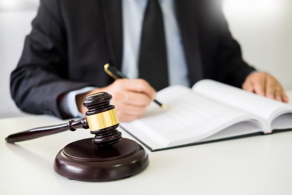 A gavel and sound block rest on a wooden desk, symbolizing justice and the law, while a lawyer works in the background.