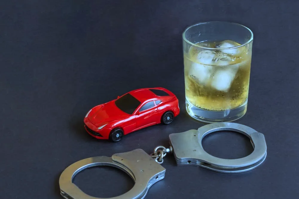 A toy car, handcuffs, and a bottle of alcohol are displayed against a colorful background, illustrating the dangers of driving under the influence.